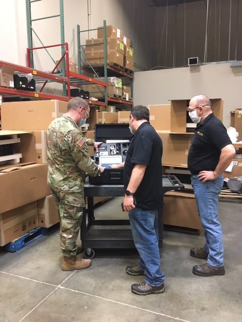 Captain Adam Hever of Army National Guard Bureau (NGB) Headquarters, Savi Technology’s Doug Schreffler and First Source Electronics’ Chris Macek inspect order of 221 Savi Portable Deployment Kits (PDKs) III at First Source Electronics’ Maryland location